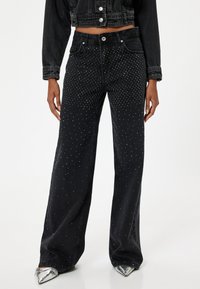 Vaqueros anchos negros con adornos de strass dispuestos en un patrón de degradado; fabricados en denim con un diseño clásico de cinco bolsillos.