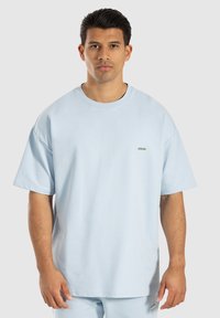 T-shirt oversize azzurro chiaro con maniche corte, scollatura rotonda e piccolo logo argento sul petto. Tessuto morbido, materiale misto cotone.