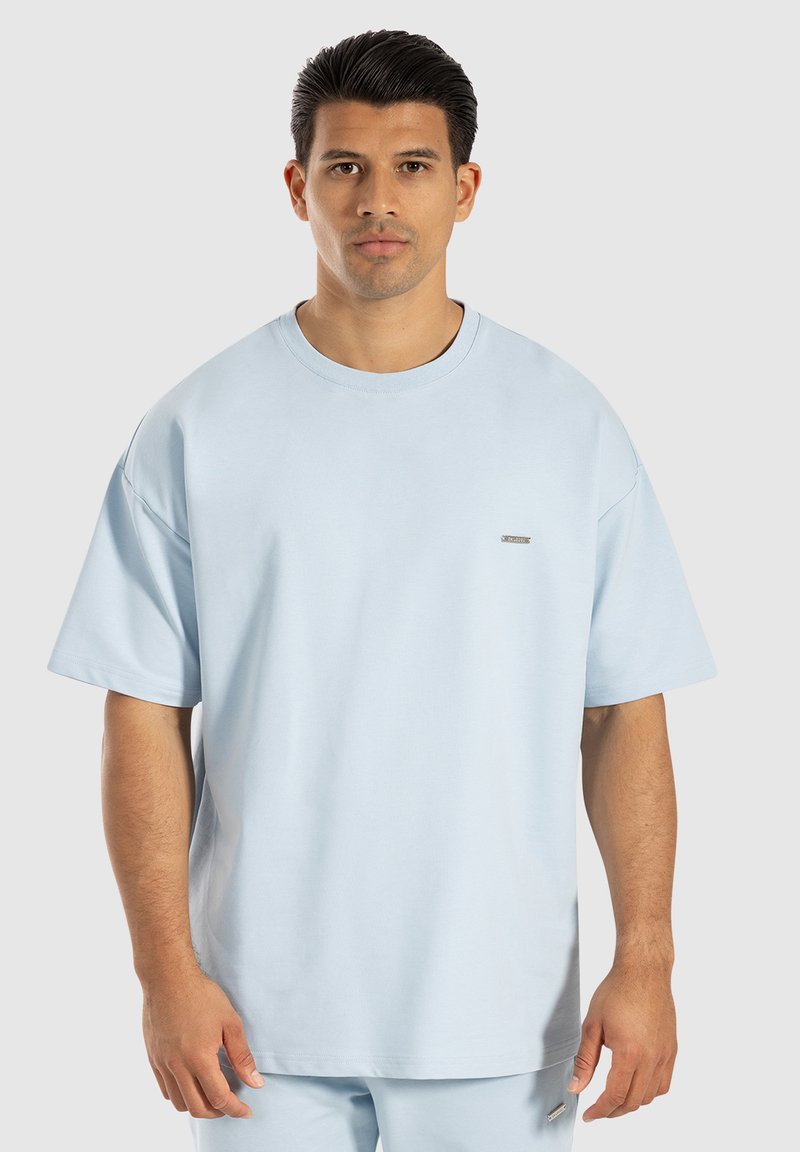 T-shirt oversize azzurro chiaro con maniche corte, scollatura rotonda e piccolo logo argento sul petto. Tessuto morbido, materiale misto cotone.