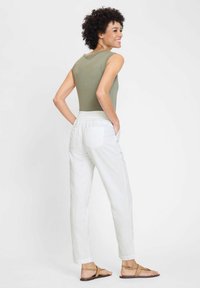 Olive green sleeveless top paired with white, loose-fitting pants. Pants have a back pocket and elastic waistband. Tan flat sandals visible.