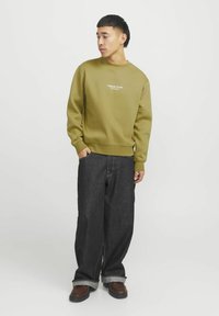 Olijfgroen sweatshirt met ronde halslijn, geribbelde mouwen en zoom, gecombineerd met wijde donkerblauwe denim jeans en bruine laarzen. Eenvoudig logo detail.