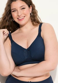 Granatowy stanik z koronkowymi akcentami i kokardką z przodu. Posiada regulowane ramiączka oraz gładką fakturę materiału.