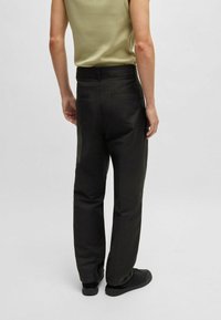 Pantalon noir à coupe droite, avec une texture lisse, des poches latérales et une taille standard, porté avec un débardeur ajusté olive.