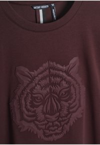 Bordo pamučna majica s uzdignutim, toniranim grafičkim prikazom tigra. Klasični kroj s okruglim izrezom i kontrastnim detaljima na etiketi.