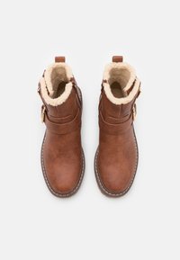 Bottines en cuir marron avec une doublure en fourrure synthétique, détail de sangle ajustable, bout arrondi et couture blanche le long de la semelle.