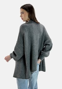 Maglione grigio oversize in maglia con maniche ampie e texture a coste. Vestibilità morbida con scollatura rotonda; indossato sopra jeans azzurri chiari.