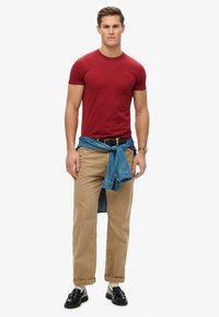 Camiseta roja de manga corta, pantalones caqui, camisa de mezclilla atada a la cintura, zapatos negros, atuendo casual con un diseño y texturas simples.