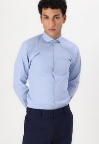 Light blue long-sleeve shirt with a pointed collar, button-down front, and smooth texture, paired with dark navy trousers.