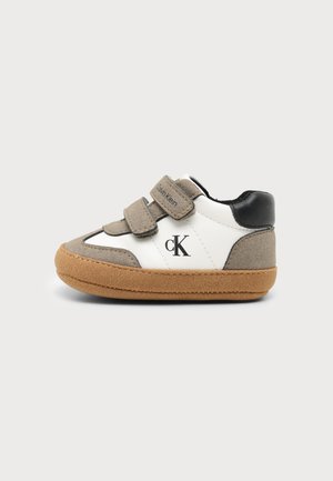 Witte en beige toddler sneaker met bruine zool, zwarte hiel, twee beige klittenbandriemen en "cK" logo aan de zijkant.