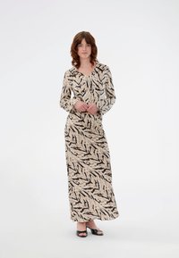 Robe longue à motifs en beige avec des rayures abstraites noires, dotée d'un décolleté en V, de manches longues et d'une silhouette fluide. Sandales noires incluses.