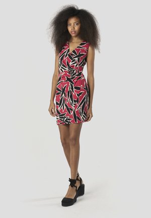 Piros ruha fekete és bézs levélmintákkal, testhez simuló fazon, átlapolt kialakítás, ujjatlan, fekete ék-pántos szandálokkal párosítva.