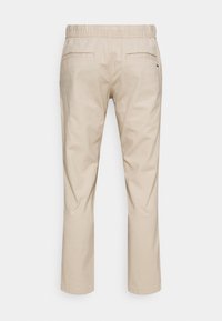 Beige Hosen mit geradem Bein, elastischem Bund und Eingrifftaschen hinten, flach von hinten auf einfachem Hintergrund dargestellt.