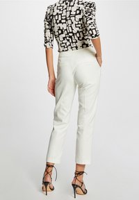 Valkoiset räätälöidyt housut, joissa on slim fit -leikkaus, sileä pinta ja kaksi takataskua, yhdistettynä musta-valkoiseen kuviolliseen yläosaan.
