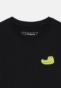Čierne detské tričko s okrúhlym výstrihom a malou jasne zelenou karikatúrou krokodílej tváre potlačenou na hrudi.