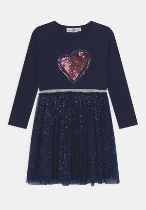 Granatowa sukienka z długim rękawem z różowym cekinowym sercem na piersi, srebrnym paskiem w talii i błyszczącą, siateczkową nakładką na spódnicę.