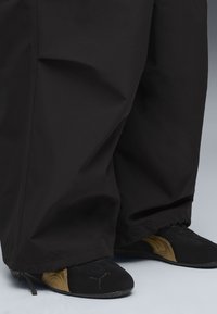 Pantaloni neri, larghi, con caviglie arricciate abbinati a scarpe da ginnastica nere e oro con superficie testurizzata e logo.
