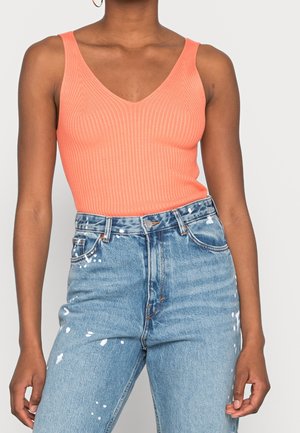 Różowa, prążkowana koszulka na ramiączkach z dekoltem w kształcie litery V, zestawiona z wysokogatunkowymi, postarzanymi niebieskimi dżinsami z akcentami farby.