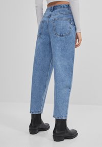 Jeans de pierna recta de talle alto en azul claro con un acabado desteñido, que presentan dos bolsillos traseros y una cinturilla sin costuras. Se llevan con botas de tobillo negras.