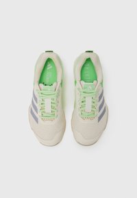 Beige athletic shoes with grey stripes and green accents. Mesh upper and cushioned sole. Lightweight design, featuring lace-up closure and branding.