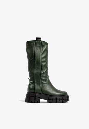 Bota alta de cuero verde oscuro con superficie texturizada, suela gruesa y robusta de color negro, lengüeta lateral para tirar y patrón de banda de rodadura resistente.
