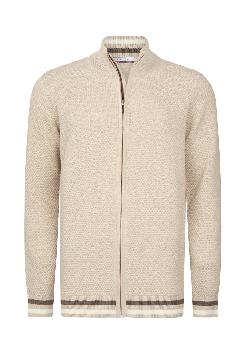 Cardigan de couleur crème avec un motif de tricot texturé, fermeture éclair et poignets côtelés avec des rayures brunes et blanches. Design à col haut.