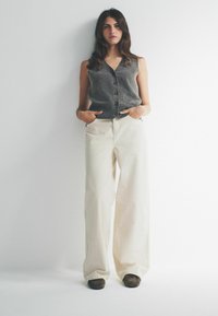 Šedý pletený sveter s gombíkmi, spárovaný s béžovými širokými nohavicami a hnedými šľapkami. Textúrovaná tkanina a uvoľnený strih.