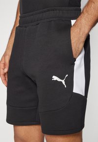 Svart sportslige shorts med en glatt tekstur, med et hvitt sidestykke og en hvit Puma-logo på venstre bein. Elastisk midjebånd inkludert.