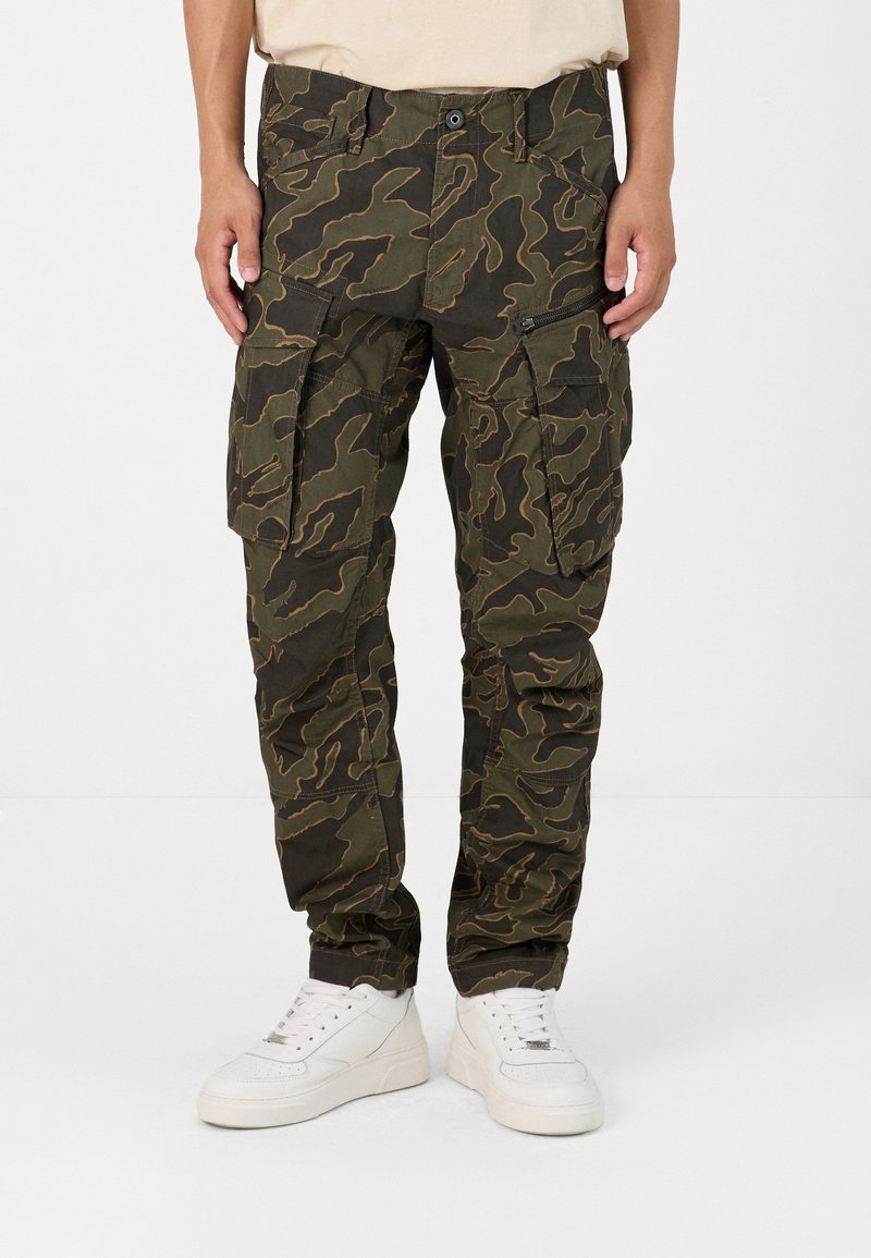 Camouflage cargo broek in donkergroen met bruine wervelingen; kenmerken zijn onder andere meerdere zakken, ritsaccenten en een relaxed fit.