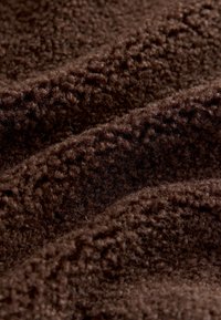 Tissu brun duveteux avec une surface texturée, présentant des fibres douces et denses disposées en plis ondulés, créant une apparence moelleuse.