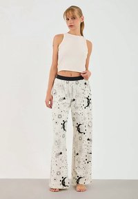 Calças de pijama brancas com padrões celestiais pretos, incluindo luas e estrelas, combinadas com uma blusa de alça justa clara. Tecido suave, ajuste relaxado.