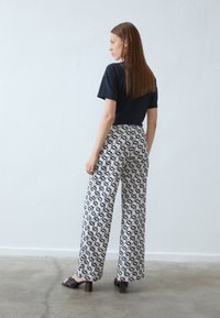T-shirt noir à manches courtes associé à un pantalon blanc avec un motif géométrique noir et des jambes larges ; mannequin portant des sandales à talons noires.