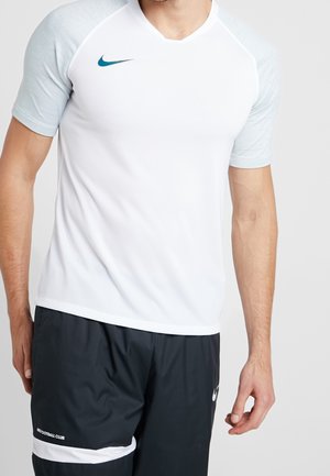 Mann trägt weißes sportliches Kurzarmshirt mit grauen Ärmeln und schwarze Sportshorts mit weißem Streifen und Nike-Logos.