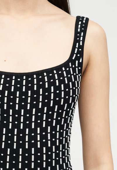 Γυναίκα που φοράει μαύρο αμάνικο τοπ με λεπτές λευκές κάθετες διακεκομμένες γραμμές, που δείχνει τον ώμο, τον λαιμό και μέρος του άνω βραχίονα.