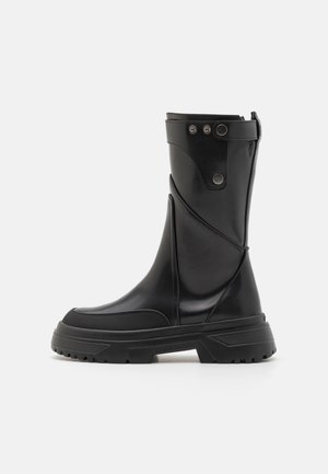 Czarne gumowe buty sięgające do kolan o matowym wykończeniu, z grubą podeszwą, zakrzywionymi akcentami wzorniczymi oraz metalowymi napami z boku do zapięcia.