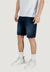 Shorts en denim noir à coupe droite, dotés de coutures contrastantes, de poches latérales et d'une taille avec passants de ceinture. Associés à des baskets blanches.