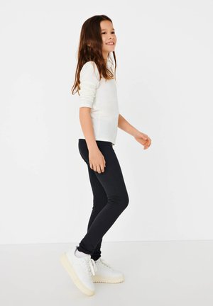 Leggings pretos combinados com uma camisa de mangas longas branca. O conjunto apresenta um corte slim e é complementado por ténis brancos com solas texturizadas.
