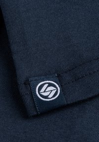Marine stof met een gladde textuur heeft een klein geweven label met een wit logo. De stiksels zijn netjes en consistent langs de randen.