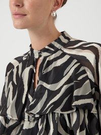Mustikkapohjainen ja beige tiikeriraidallinen paita, jossa on korkea kaulus ja kerroksellinen rypytysdesign. Sisältää sydämenmuotoisen aukon ja läpikuultavan tekstuurin.