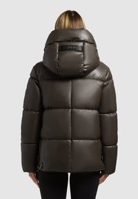 Tamsiai rudas pūkinis džemperis su blizgiu paviršiumi, su dideliu gobtuvu, kvadratiniais siūlais ir logotipu nugaroje prie kaklo.