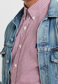 Röd och vit rutigt knapp-up skjorta bärs under en ljusblå denimjacka med metallknappar.