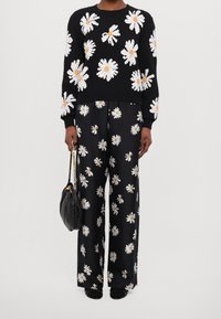 Stickad svart tröja med vita prästkrageprydnader, kombinerad med vida svarta byxor med ett liknande blommönster. Svart handväska som accessoar.