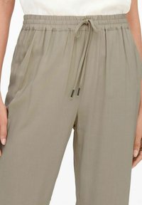 Zbliżenie beżowych spodni z elastycznym pasem i wiązanym sznurkiem z przodu, noszonych przez osobę, której ręce spoczywają blisko boków.