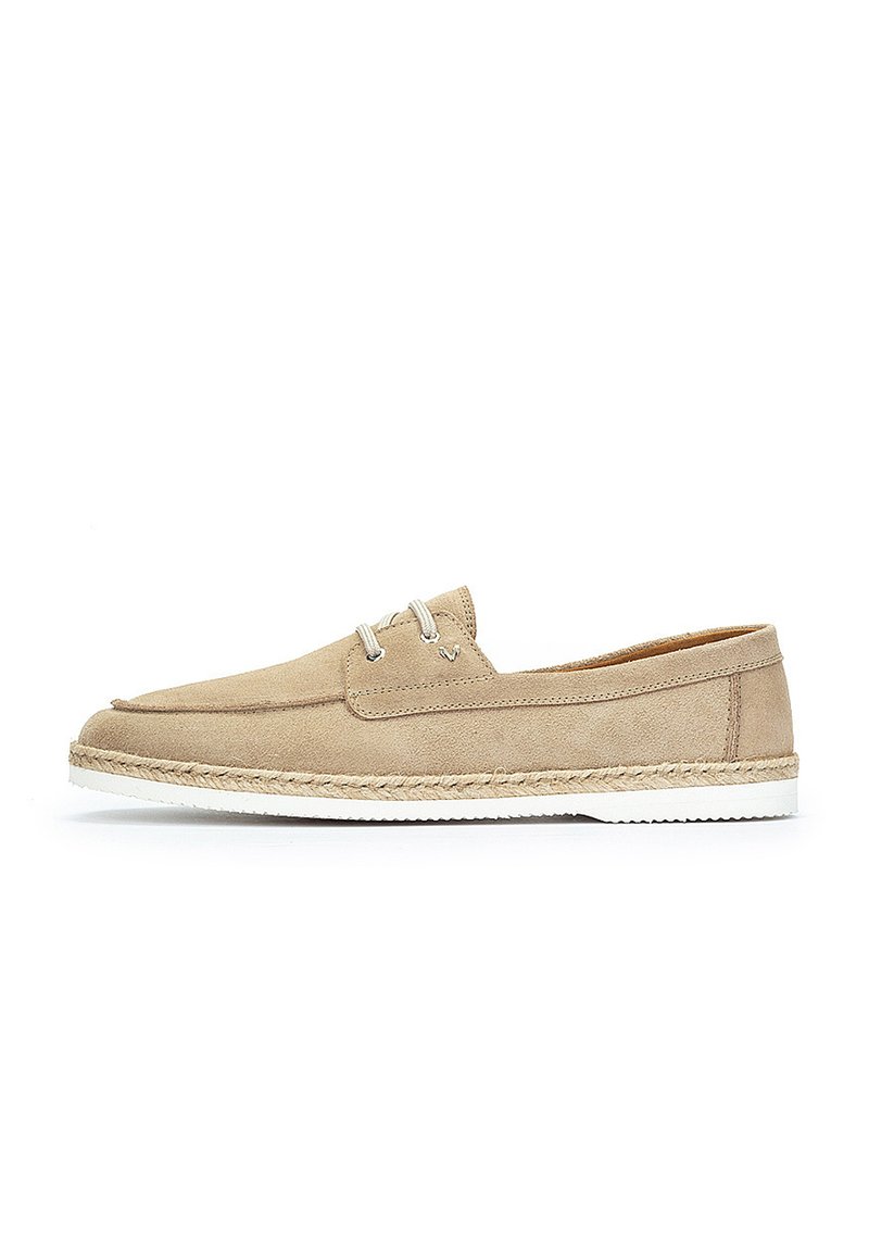 Zapato de ante beige con un diseño plano, suela de goma blanca y punta suave y redondeada. Presenta ojales de metal y un detalle de yute tejido alrededor de la suela.