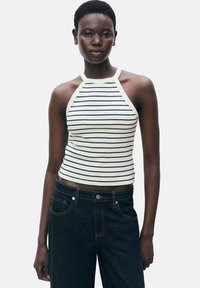 White and navy striped halter neck tank top with a fitted design, made from a soft fabric. Paired with dark denim jeans.
