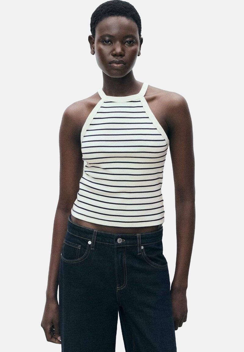 White and navy striped halter neck tank top with a fitted design, made from a soft fabric. Paired with dark denim jeans.
