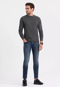 Tmavě šedá košile s dlouhým rukávem v kombinaci s modrými slim-fit džíny a černými teniskami. Tkanina vypadá hladce, bez viditelných vzorů.