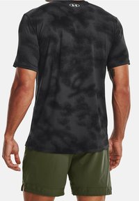 Man wearing black camo-pattern athletic t-shirt and olive green shorts, shown from the back against a white background.