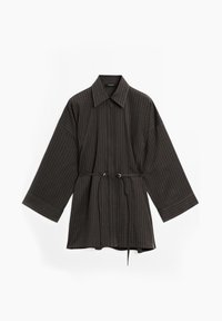 Chemise à rayures brunes foncées, à manches longues, avec des poignets larges, un col pointu et un lien de taille ajustable sur fond blanc.