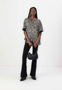 Större topp i snakeprint i grått och svart, kombinerad med svarta utsvängda byxor och en liten svart handväska med silverdetaljer.