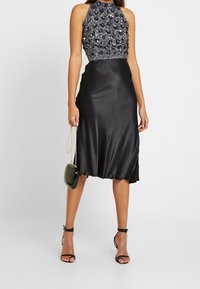 Black satin dress with a halter neck, featuring a beaded bodice. The skirt flows gently and is complemented by strappy black heels and a small handbag.